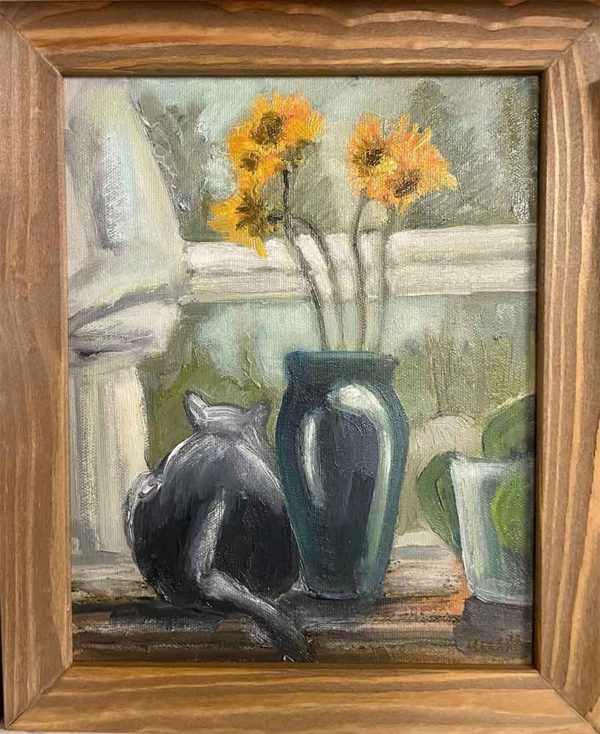 A black cat seated watching wildlife out the window, next to a blue vase with yellow flowers